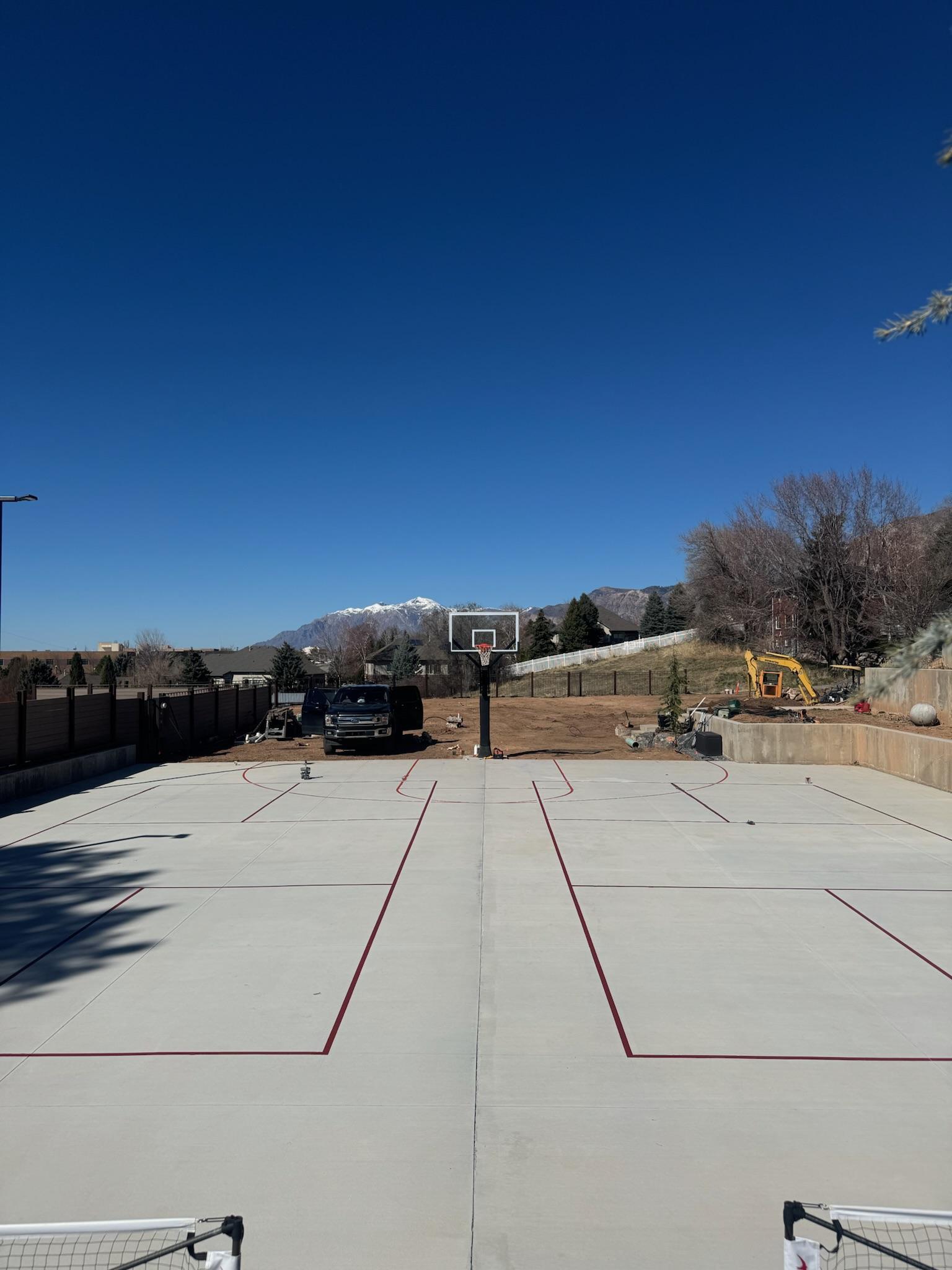 Large concrete pad with two pickleball courts and basketball lines striped in burgundy, mountains behind
