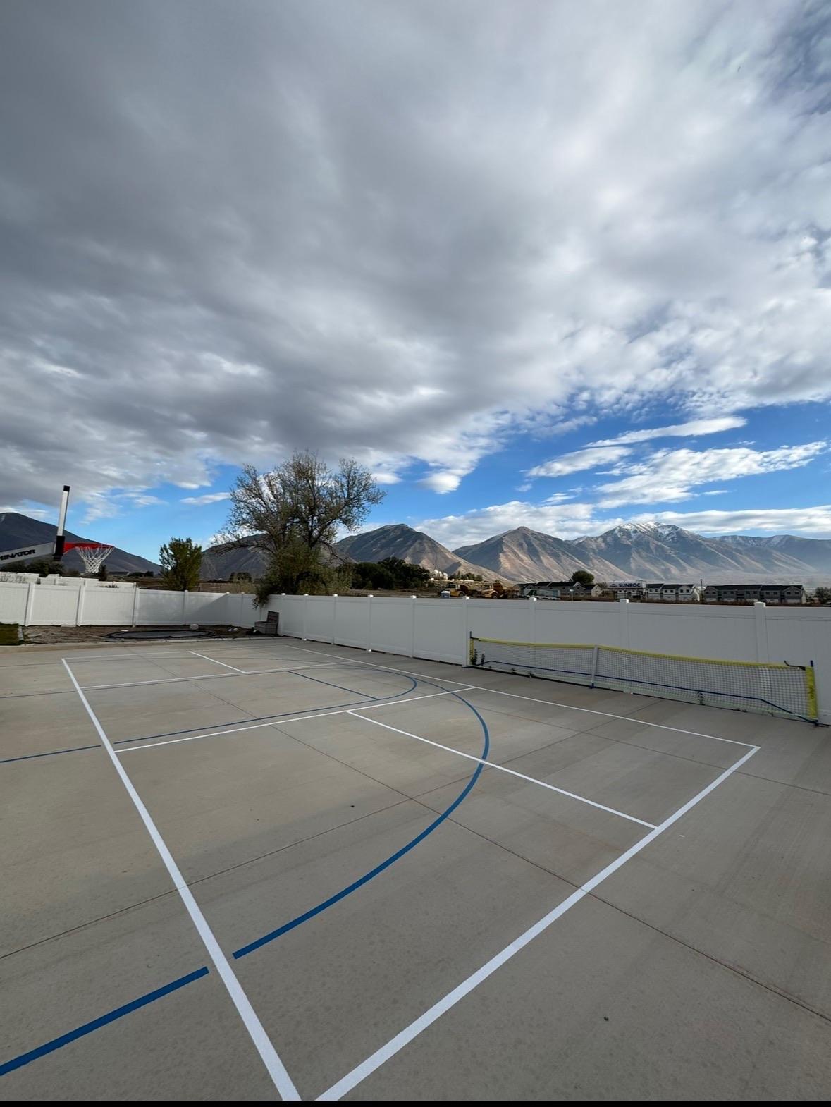 Concrete pad with white pickleball lines and blue basketball arc, hoop and mountain range behind