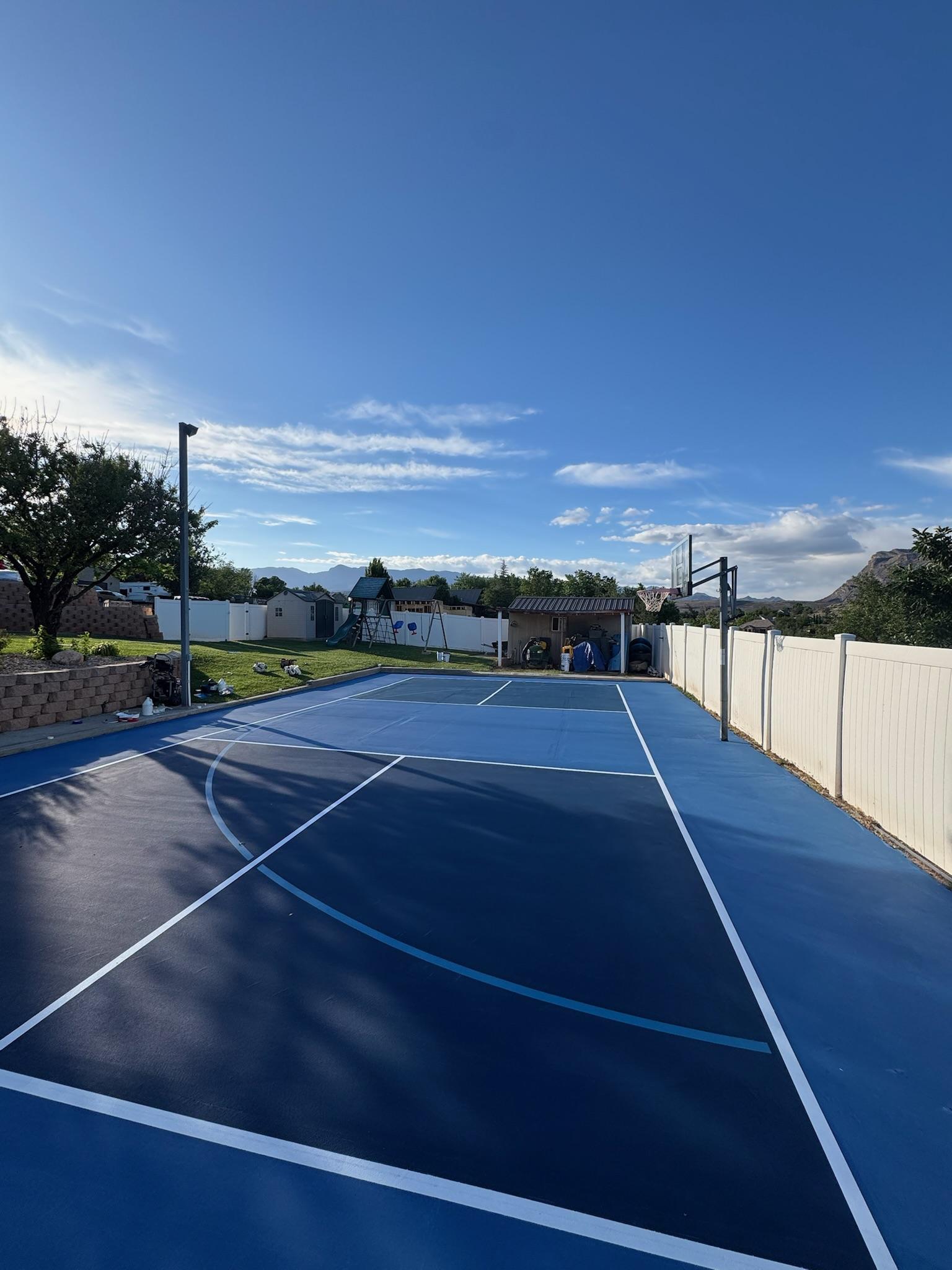 Wide view of a navy and blue multi-sport court along a white vinyl fence in a desert yard