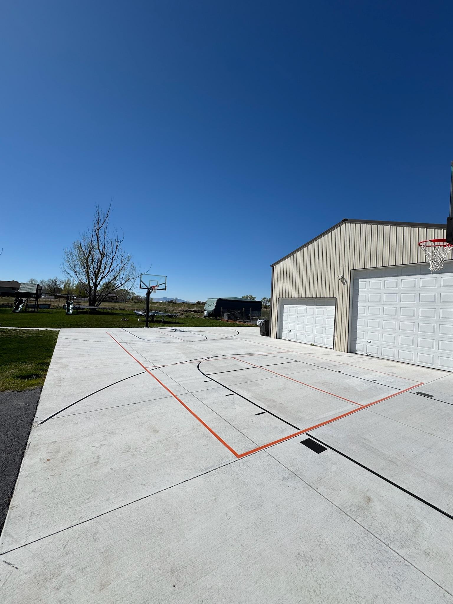 Concrete driveway beside a metal shop with black basketball lines and orange pickleball lines