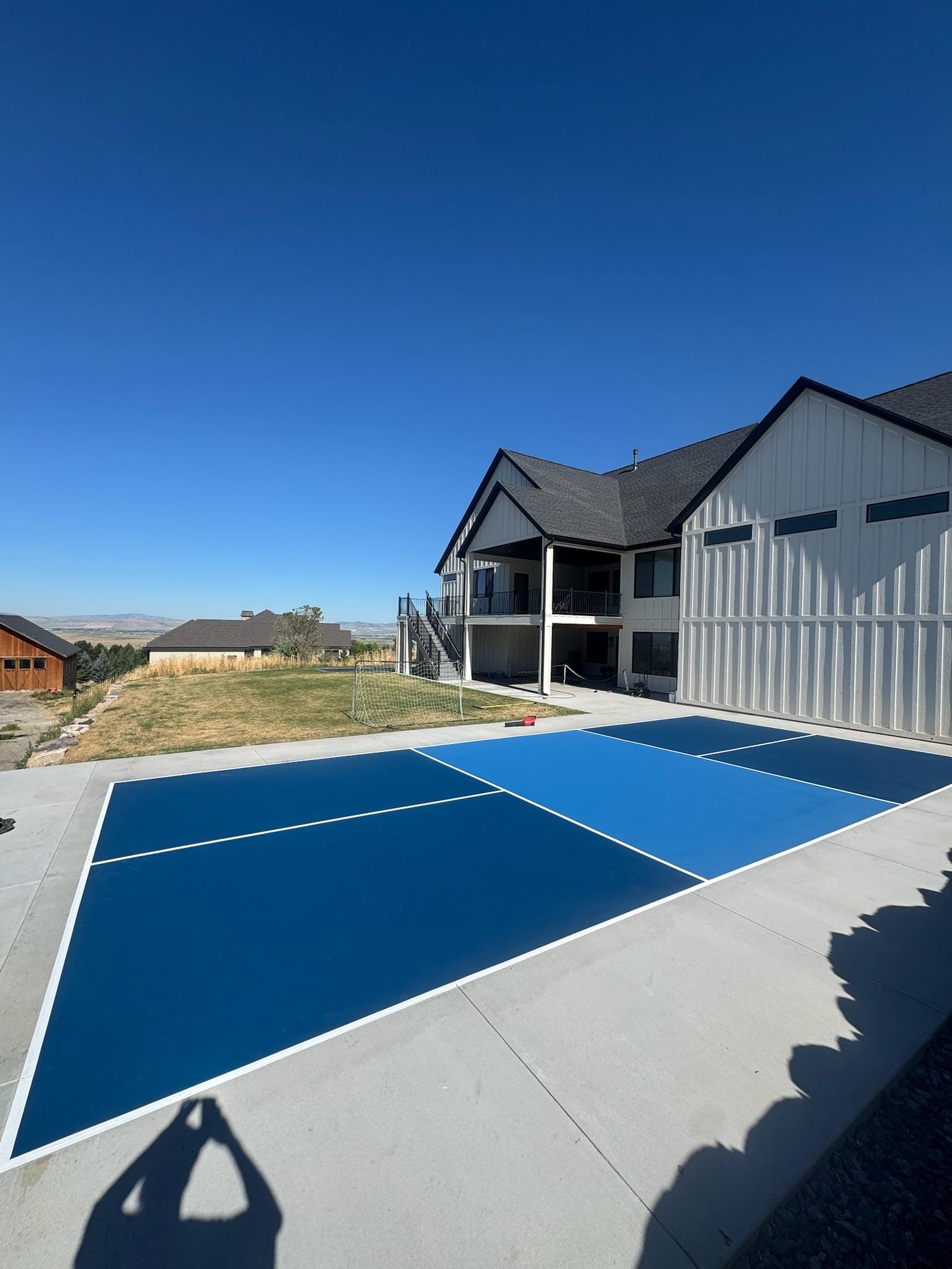 Navy and blue pickleball court on a concrete pad beside a white modern farmhouse overlooking a valley