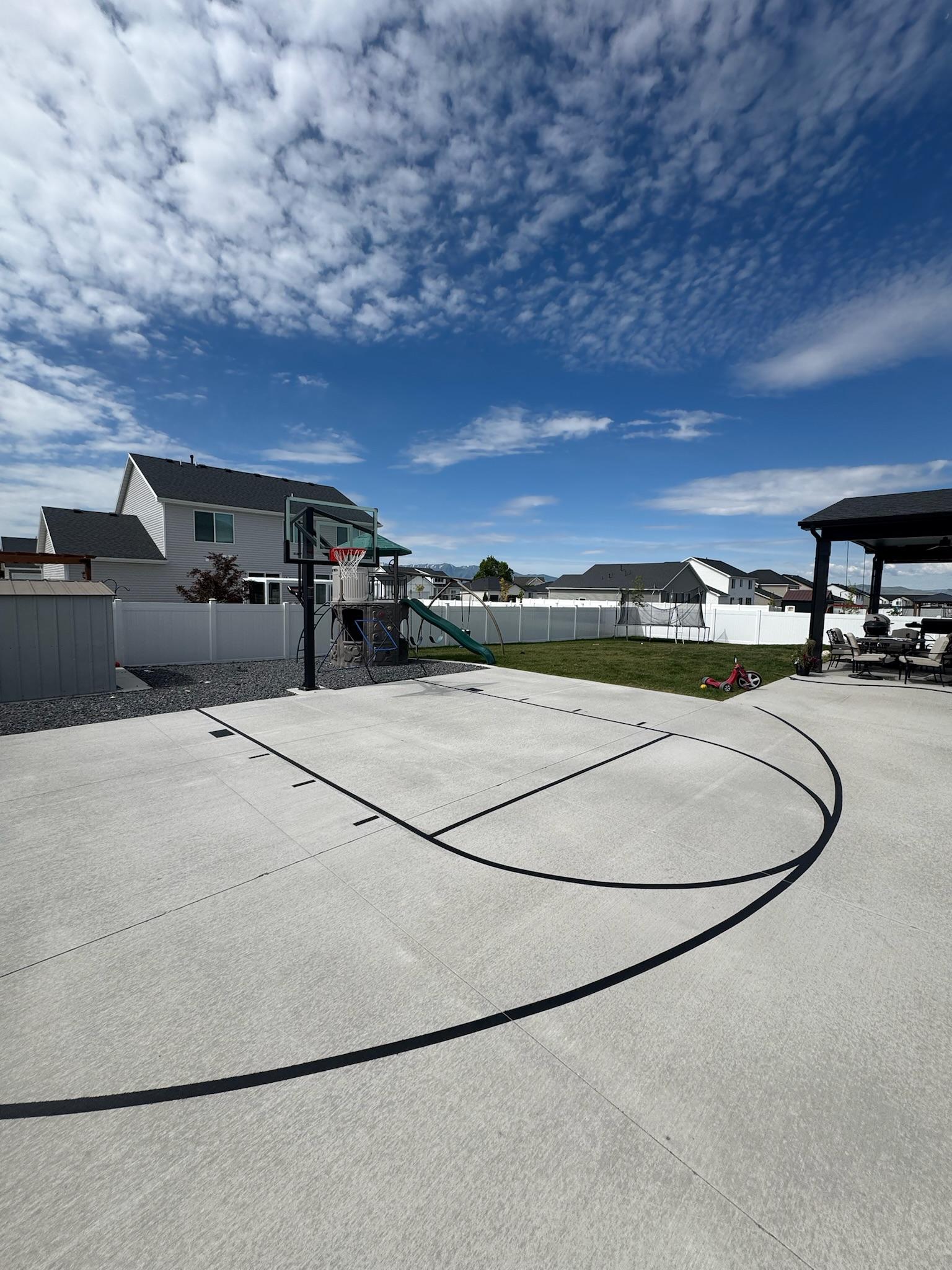 Black basketball half-court lines and hoop on new white concrete in a fenced suburban backyard