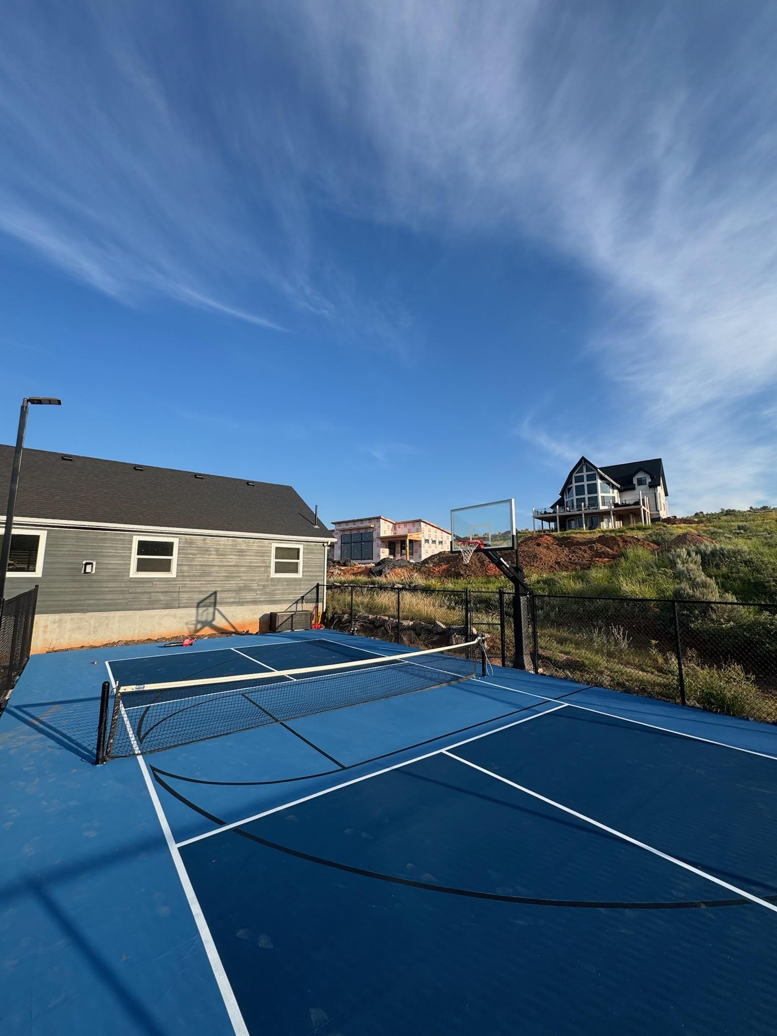 Blue two-tone multi-sport court with black basketball lines and net on a hillside among new construction