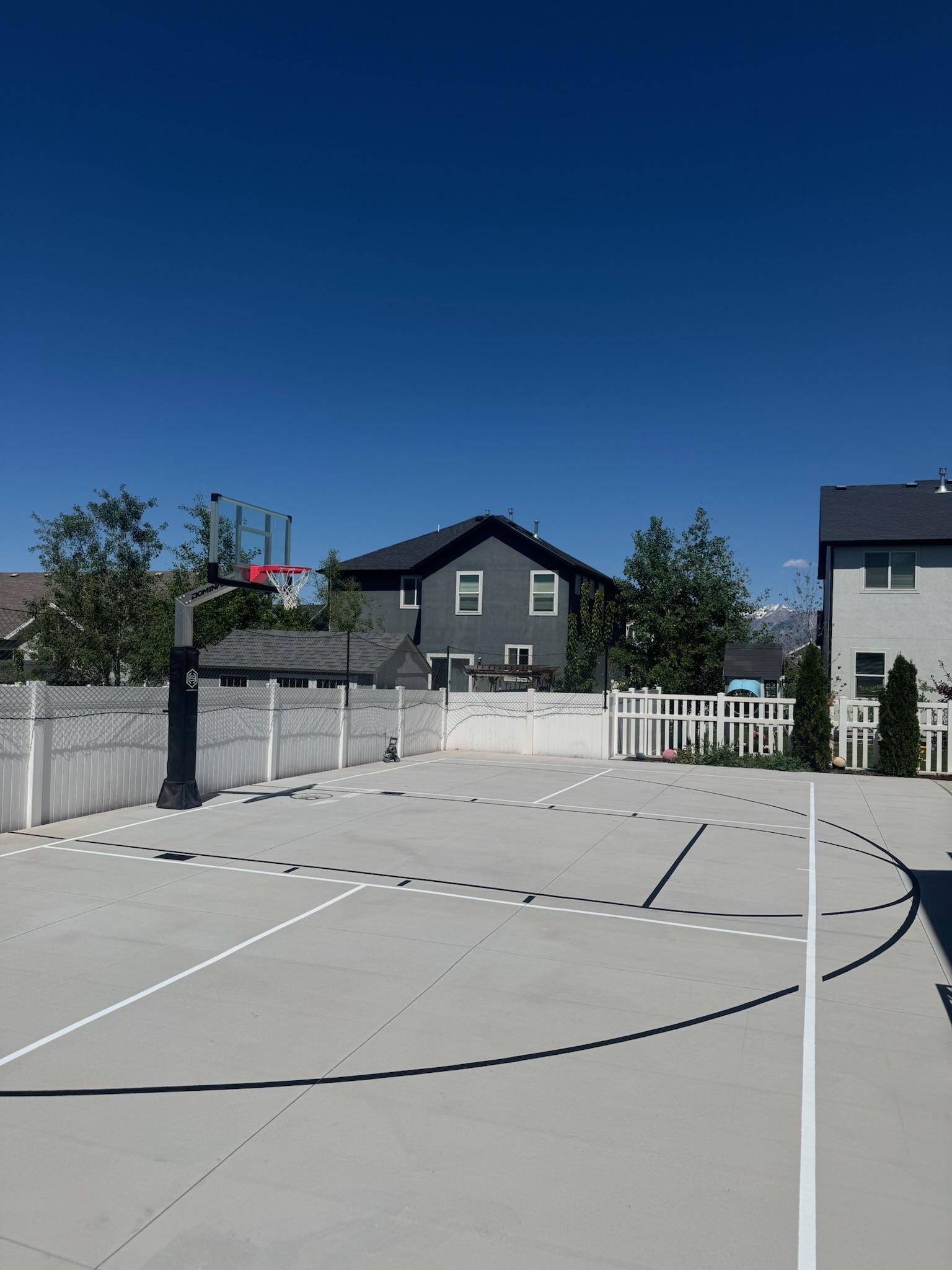 New concrete pad with black basketball lines and white pickleball lines, white picket fence behind