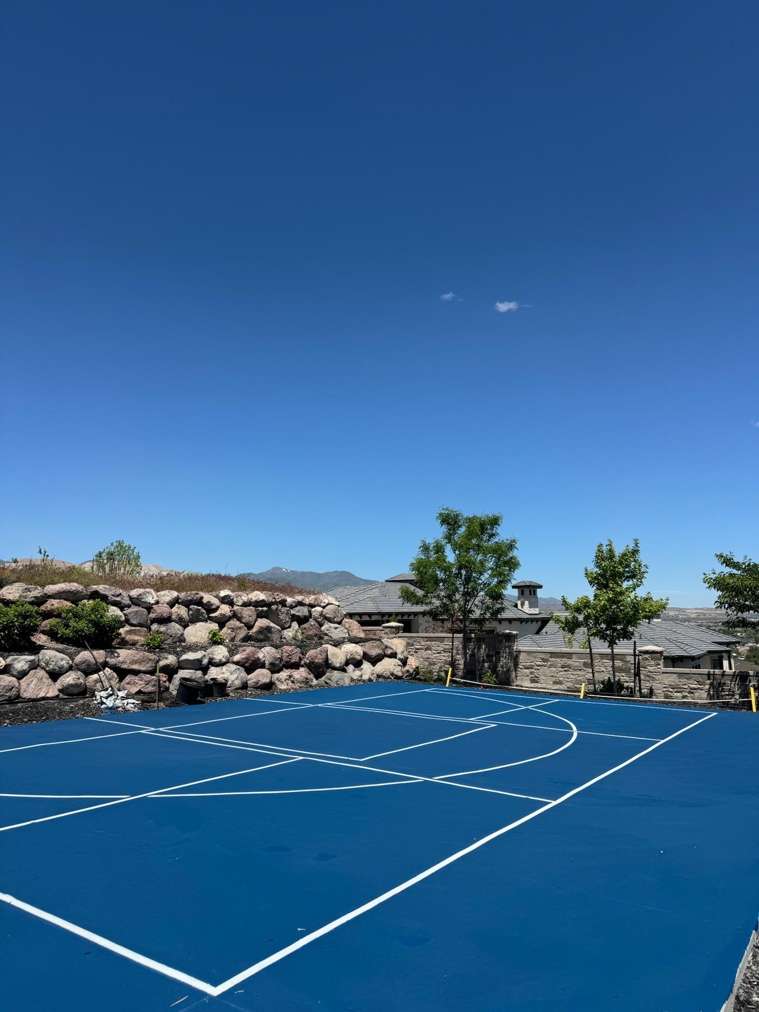 Royal blue multi-sport court with white basketball and pickleball lines beside a boulder retaining wall