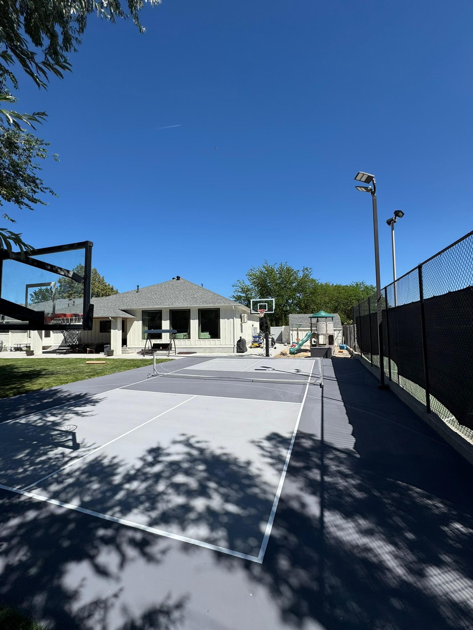 Gray two-tone pickleball court with white lines, court lights, and black privacy fence