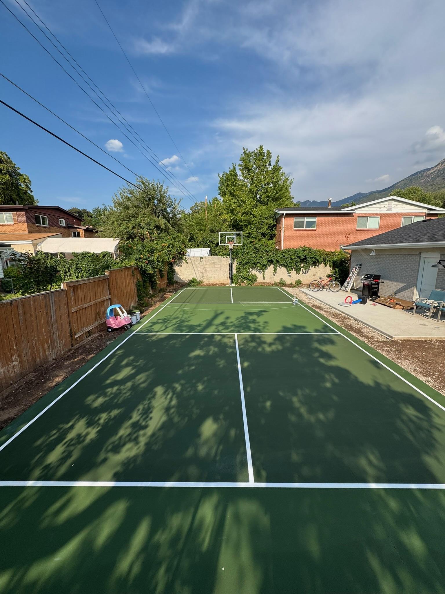Forest green and olive two-tone backyard court with white lines and basketball hoop against a vine-covered wall